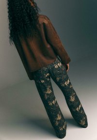 Giacca di pelle marrone con una vestibilità comoda abbinata a pantaloni a gamba larga con un audace motivo astratto in nero e crema. Tessuto testurizzato visibile.