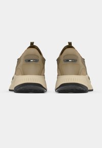 Μπεζ αθλητικά παπούτσια με υφή στην επάνω επιφάνεια, επενδυμένο κολάρο και αντίθετη σόλα από καουτσούκ με αυλακωτά σχέδια. Δύο ανακλαστικές λεπτομέρειες στο πίσω μέρος.