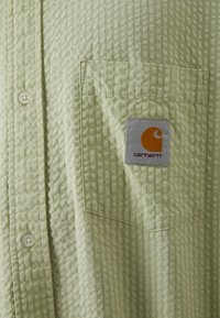 Lichtgroen overhemd met knopen, voorzien van een textuur in wafelpatroon, met een borstzak en een Carhartt logo patch in oranje en grijs.