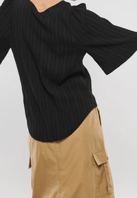 Sort, riflet bluse med V-udskæring, puffede korte ærmer og buet kant, parret med en beige cargo-nederdel med sidelommer.