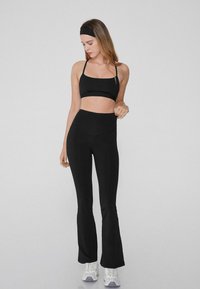 Soutien-gorge de sport noir et leggings évasés taille haute en tissu extensible, avec un design minimaliste. Des chaussures de sport blanches complètent la tenue.