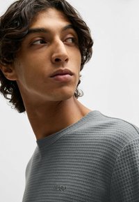 Grijze textuur T-shirt met een ronde halslijn, voorzien van subtiele branding op de borst. Zachte stof met een geweven patroon voegt diepte toe.