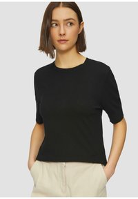 Schwarzes T-Shirt mit kurzen Ärmeln aus einem weichen, strukturierten Stoff. Mit Rundhalsausschnitt und lockerer Passform, kombiniert mit hellen Hosen.