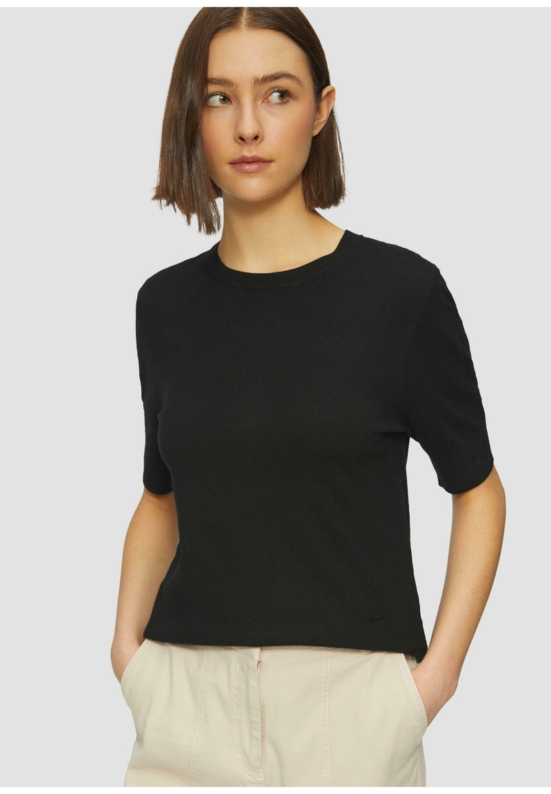 Schwarzes T-Shirt mit kurzen Ärmeln aus einem weichen, strukturierten Stoff. Mit Rundhalsausschnitt und lockerer Passform, kombiniert mit hellen Hosen.