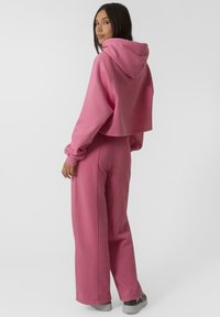 Hoodie court rose avec des manches longues et une capuche à cordon, associé à un pantalon large rose. Tissu doux avec des détails de couture visibles.