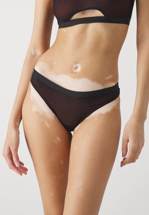 Black polka dot bikini set with cut-out details, matching elastic waistband, soft texture, and low-rise design. Skin with lighter areas visible.