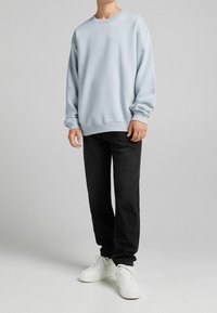 Vaaleansininen collegepaita, jossa on pyöreä kaula-aukko, ribbetyt hihansuut ja helma, yhdistetty mustiin farkkuihin ja valkoisiin tennareihin. Sujuva rakenne, rento istuvuus.