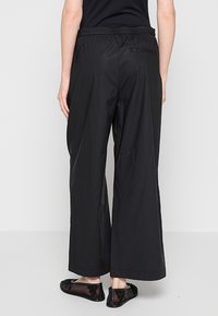 Schwarze Hosen mit weitem Bein und elastischem Bund, gefertigt aus einem glatten, leichten Stoff. Auf der rechten Seite ist eine Gesäßtasche sichtbar.