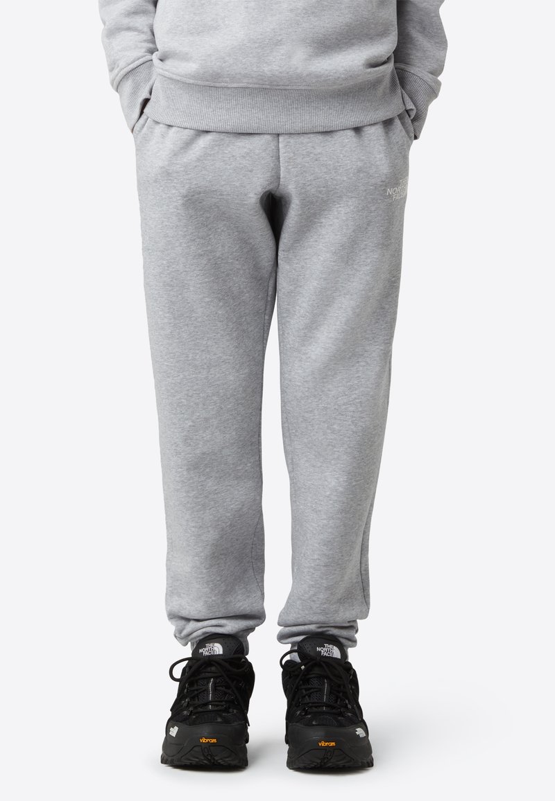 Grå joggebukser i et mykt stoff med elastisk midjebånd. Kombinert med svarte treningssko med teksturerte såler og logodetaljer.