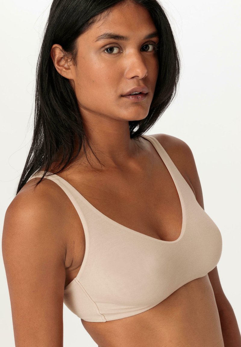 Beige bralette gemaakt van zachte, rekbare stof. Heeft een V-halsontwerp en dunne bandjes, wat zorgt voor een gladde, naadloze uitstraling.