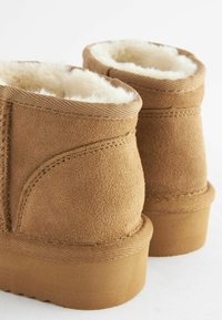 Tan ruskind ankle boots med en blød, hvid pelsforing, der har dekorativ syning og en struktureret gummisål.