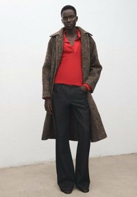 Abrigo de mezcla de lana en marrón con solapa en contraste, combinado con una camiseta roja de canalé y pantalones anchos oscuros, mostrando un acabado texturizado.