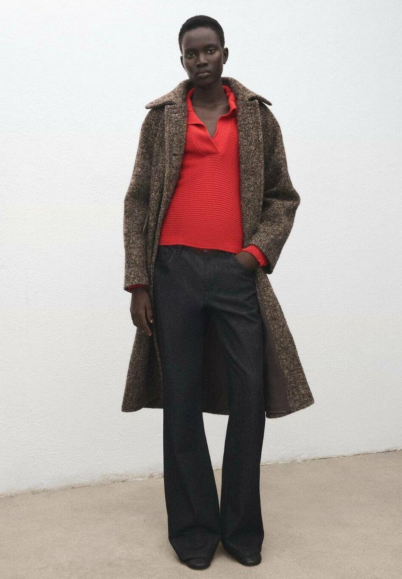 Abrigo de mezcla de lana en marrón con solapa en contraste, combinado con una camiseta roja de canalé y pantalones anchos oscuros, mostrando un acabado texturizado.