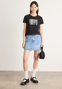 T-shirt in cotone nero con "DKNY" stampato in argento, abbinato a una gonna di jeans azzurro chiaro, calzini bianchi e scarpe Mary Jane nere. Piccola borsa nera.