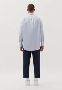 Camicia azzurra a righe con una vestibilità rilassata, polsini confezionati e orlo arrotondato, abbinata a pantaloni blu navy e sneakers bianche.