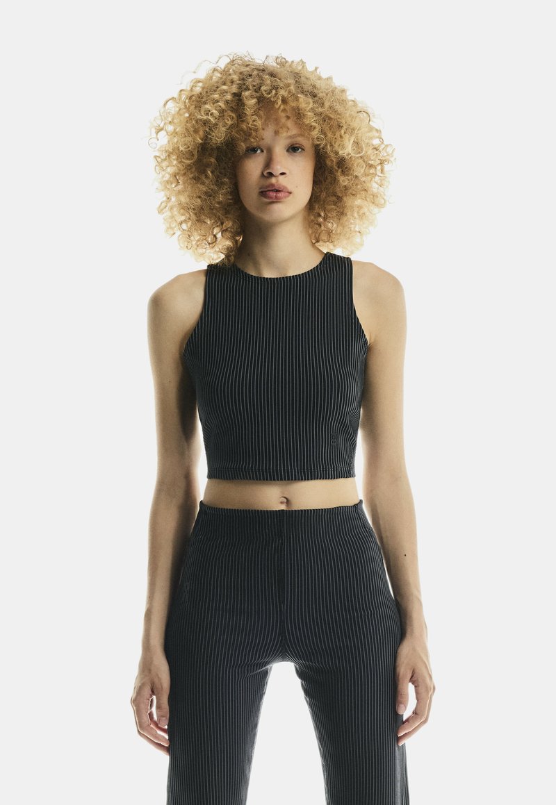 Ciemnoniebieski prążkowany crop top z wysokim dekoltem, zestawiony z dopasowanymi spodniami o wysokim stanie z podobnym wzorem prążków.