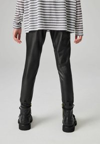 Pantaloni in pelle nera dal design elegante, abbinati a stivaletti neri alla caviglia con zip. La parte superiore è grigia con righe orizzontali.