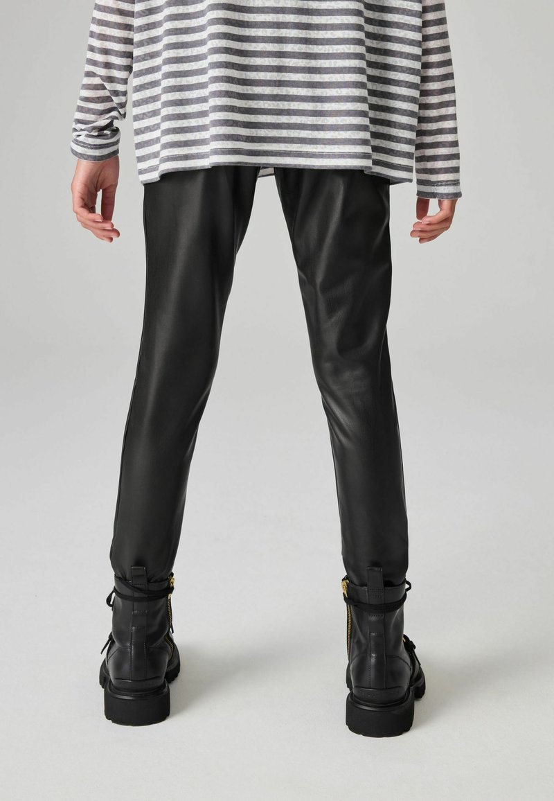 Pantaloni in pelle nera dal design elegante, abbinati a stivaletti neri alla caviglia con zip. La parte superiore è grigia con righe orizzontali.