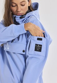 Helles blaues Kapuzensweatshirt mit einer frontalen Tasche, gerippten Bündchen und einem schwarzen Etikett mit weißem Text auf dem linken Ärmel. Glatte Textur.