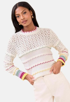 White knitted sweater with openwork pattern, scalloped edges, and multicolored striped cuffs in pink, green, blue, and yellow.
