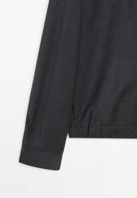 Long dark grey sleeve with elastic cuff and subtle textured fabric.