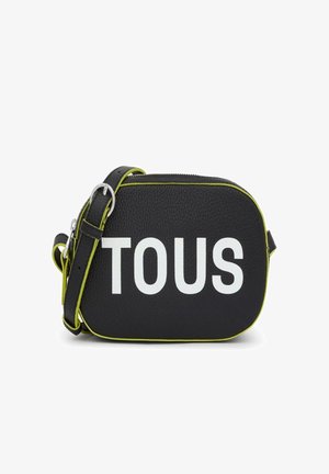 Bolso cruzado de cuero negro con el texto en relieve "TOUS" en blanco. Presenta acentos en verde lima y una correa desmontable. Acabado de textura suave.