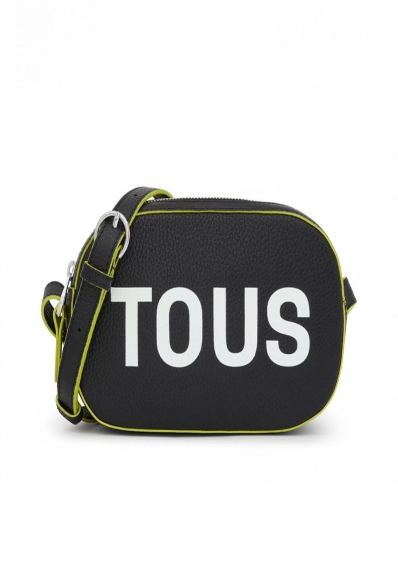 Bolso cruzado de cuero negro con el texto en relieve "TOUS" en blanco. Presenta acentos en verde lima y una correa desmontable. Acabado de textura suave.