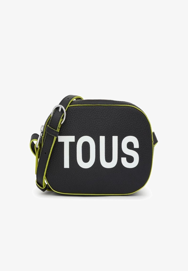 Bolso cruzado de cuero negro con el texto en relieve "TOUS" en blanco. Presenta acentos en verde lima y una correa desmontable. Acabado de textura suave.