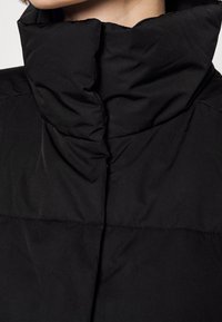 Czarna puchowa kurtka z wysokim kołnierzem, o gładkiej fakturze i poziomych przeszyciach. Prosty, funkcjonalny design.