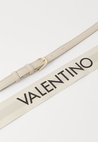 Beige lærrem med en gullfarget metallspenne; inkluderer et kremfarget stoffmerke med "VALENTINO" i fet svart skrift.