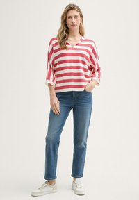 Top a righe rosse e bianche con scollatura a V, caratterizzato da maniche a tre quarti, abbinato a jeans a gamba dritta blu e sneakers bianche.