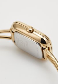 Gold-tone wristwatch with a rectangular case, side crown, and a smooth polished finish. Features a shiny metal strap and a silver case back.