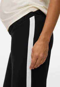 Czarne dresy z białym pionowym pasem po boku, charakteryzujące się luźnym krojem i elastycznym pasem w talii. Gładki materiał bawełniany.