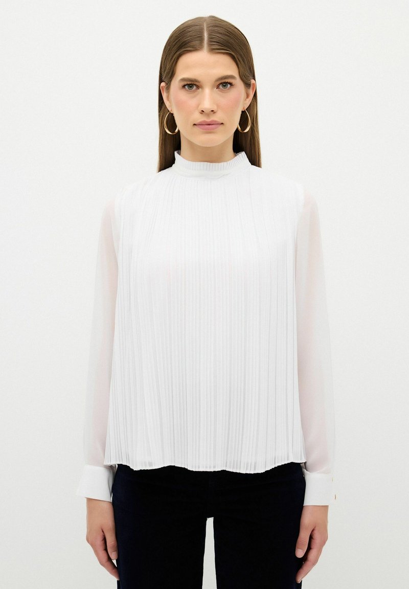 Weiße Bluse mit hohem Kragen, langen durchsichtigen Ärmeln und vertikalen Falten. Der Saum ist geschwungen, mit knöpfbaren Manschetten und einer glatten Textur.