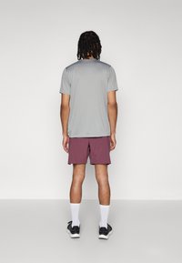 Grå kortermet treningsskjorte og bordeauxshorts. Modell som har på seg hvite sokker og svarte joggesko, sett fra ryggen. Enkelt design.