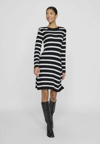 Robe à manches longues bicolore rayée en noir et blanc avec un corsage ajusté et un bas évasé, présentant des boutons décoratifs sur l'épaule et une texture côtelée.