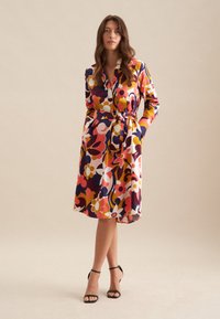Blumendruckkleid in verschiedenen Farben mit langen Ärmeln, einem taillierten Bund und einem knielangen Saum; glattes Material mit glänzender Oberfläche.