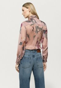 Sheer pink blouse with floral pattern, long sleeves, and a straight cut, paired with high-waisted denim jeans featuring back pockets.