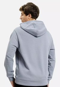 Szara bluza z kapturem o miękkiej fakturze, z regulowanym kapturem, ściągaczami przy rękawach i dolnym wykończeniu, noszona przez modela prezentującego widok z tyłu.