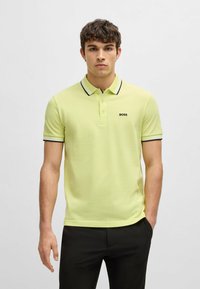 Pikétröja i klar gul färg, med en svart och vit randig krage och manschettdetaljer. Broderad "BOSS"-logotyp på bröstet.