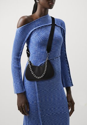 Černá ramenní taška s řetízkovým popruhem, spárovaná s modrým žebrovaným šaty s designem bez ramene a knoflíkovými detaily.