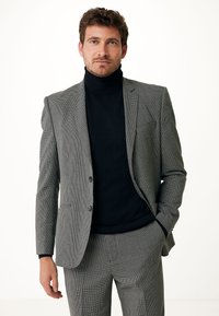 Giacca da suit a motivo houndstooth grigio sopra un dolcevita nero. La giacca presenta due bottoni, rever a punta e tasche frontali. Vestibilità ordinata e su misura.
