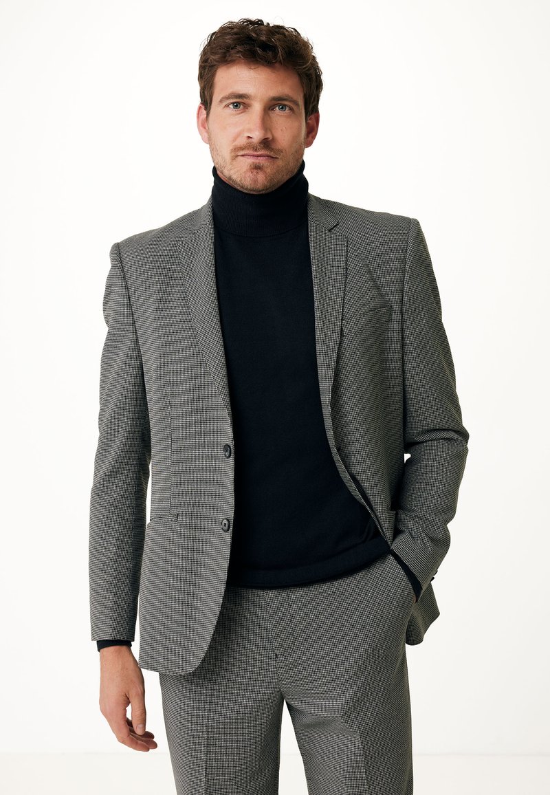 Giacca da suit a motivo houndstooth grigio sopra un dolcevita nero. La giacca presenta due bottoni, rever a punta e tasche frontali. Vestibilità ordinata e su misura.