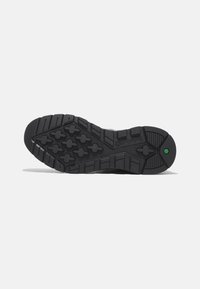 Suela de zapato de goma negra con un patrón texturizado de surcos horizontales y verticales, formas de diamante centrales y un detalle hexagonal verde.