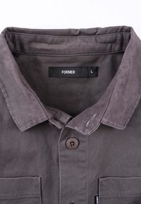 Γκρι βαμβακερό πουκάμισο με γιακά, διαθέτει δύο μπροστινές τσέπες και κλείσιμο με κουμπιά. Η ετικέτα γράφει "FORMER" με μέγεθος "L".