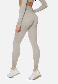 Hochtaillierte Leggings in hellbeige, aus strukturiertem Stoff mit einem Farbverlaufmuster. Kombiniert mit weißen Sportschuhen.