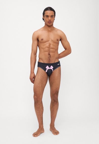 Maillots de bain noirs avec un détail de nœud rose à l'avant, fabriqués en matériau lisse. Présente une taille élastique avec un logo discret.