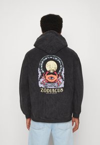 Schwarzer Hoodie mit entspanntem Schnitt, der ein farbenfrohes Zodiac-Design auf der Rückseite zeigt, einschließlich eines Krebses und eines Mondes, sowie gerippten Bündchen.