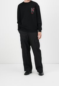 Felpa nera con un piccolo logo rosso e grigio sul petto, abbinata a pantaloni cargo neri con tasche laterali e una vestibilità rilassata.