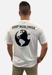 White cotton t-shirt featuring a large black globe graphic on the back, with "Gorp Worldwide" text and a tagline in black letters.